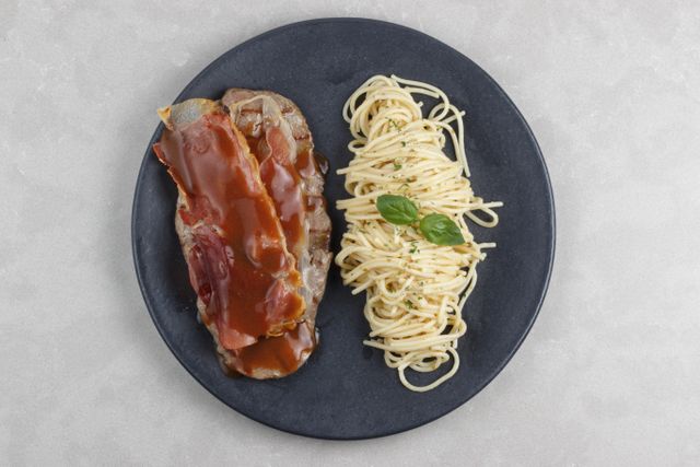 Top view of meatloaf with gravy and spaghetti garnished with basil on a black plate.