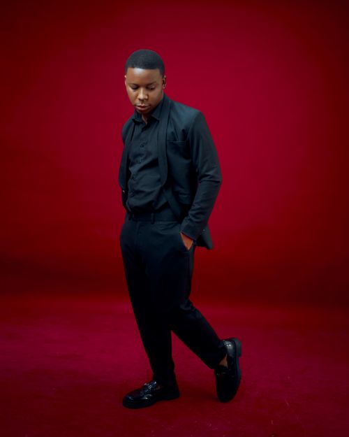 Free Fashionable portrait of a man in formal black attire against a vivid red backdrop. Stock Photo