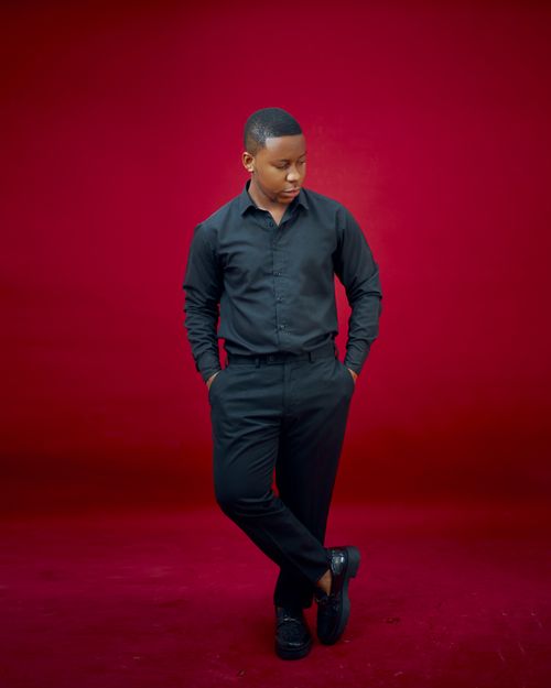 Free Elegant young adult in black attire poses confidently with a red backdrop, exuding style and poise. Stock Photo