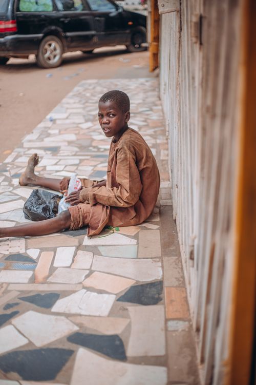 Free A young boy in casual clothing sitting outside on a tiled street sidewalk. Stock Photo