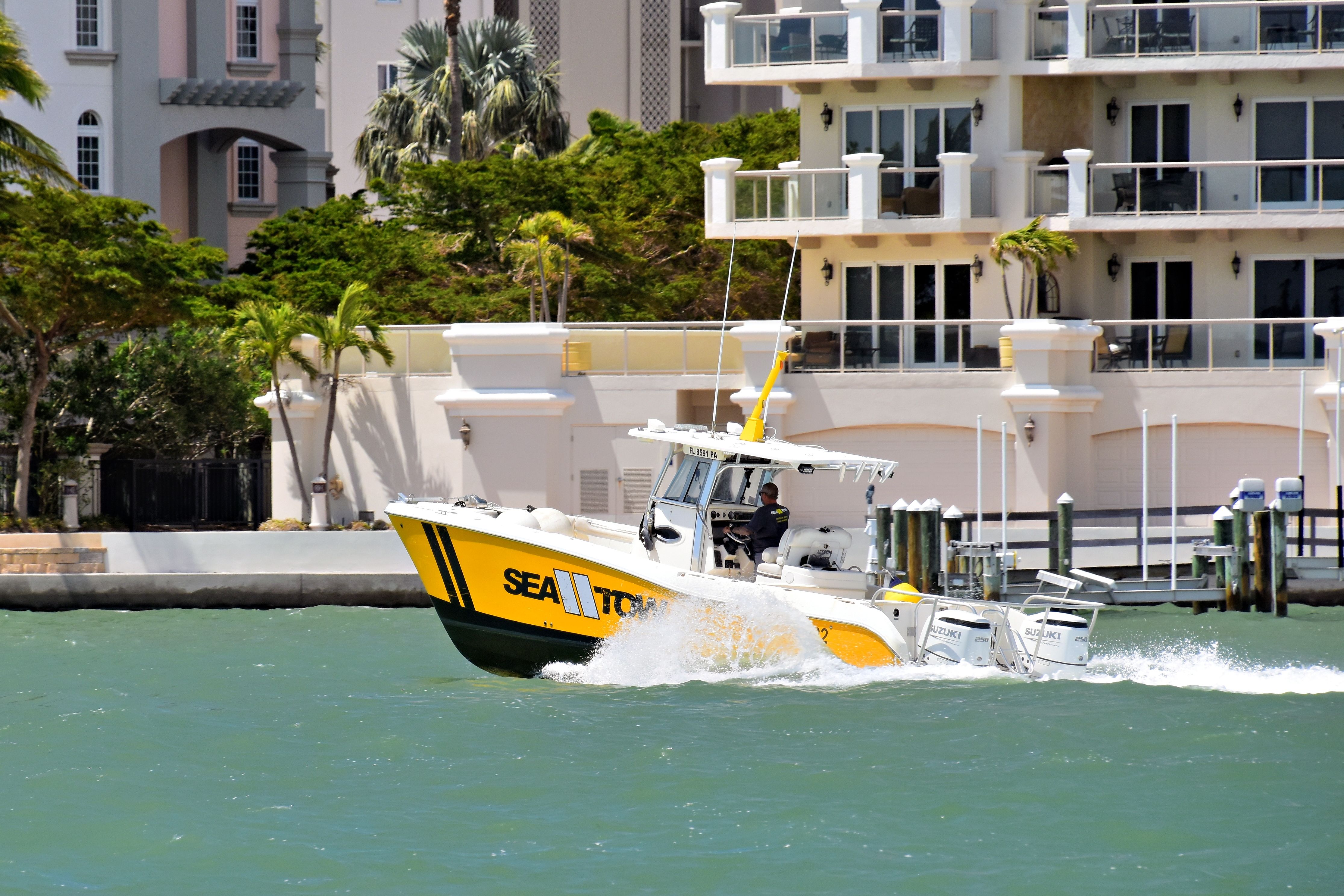A vibrant speedboat cutting through Sarasota Bay with waterfront buildings in the backdrop.