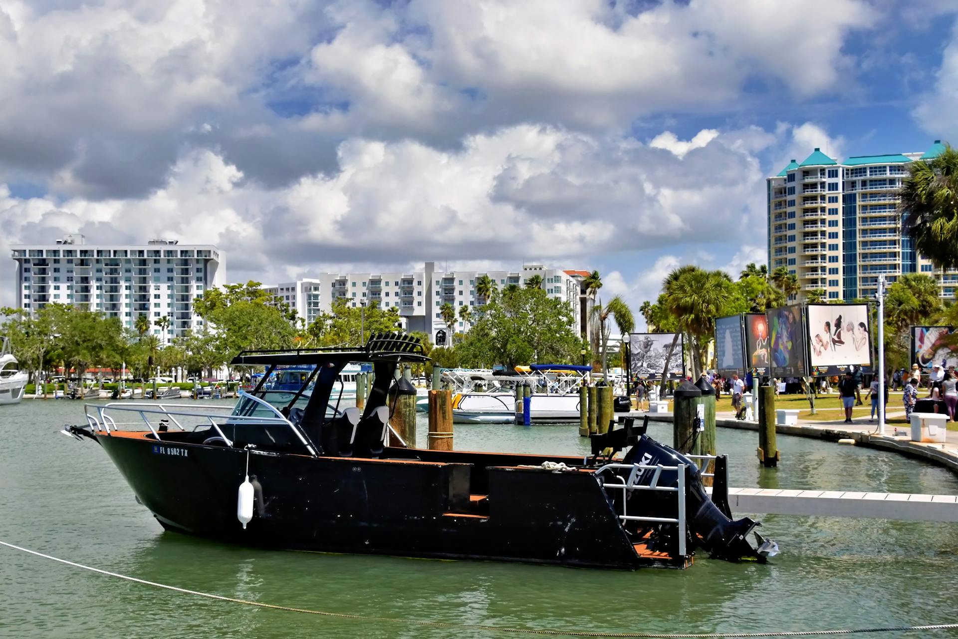 Black boat moored at Sarasota marina with city skyline and palm trees in the background.