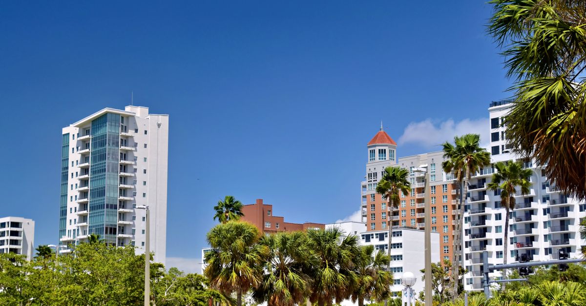 A vibrant urban scene featuring Sarasota's high-rise buildings and palm trees under a clear sky.