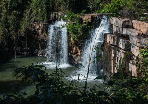 Capture the serene beauty of twin waterfalls cascading in a lush Thai jungle setting.