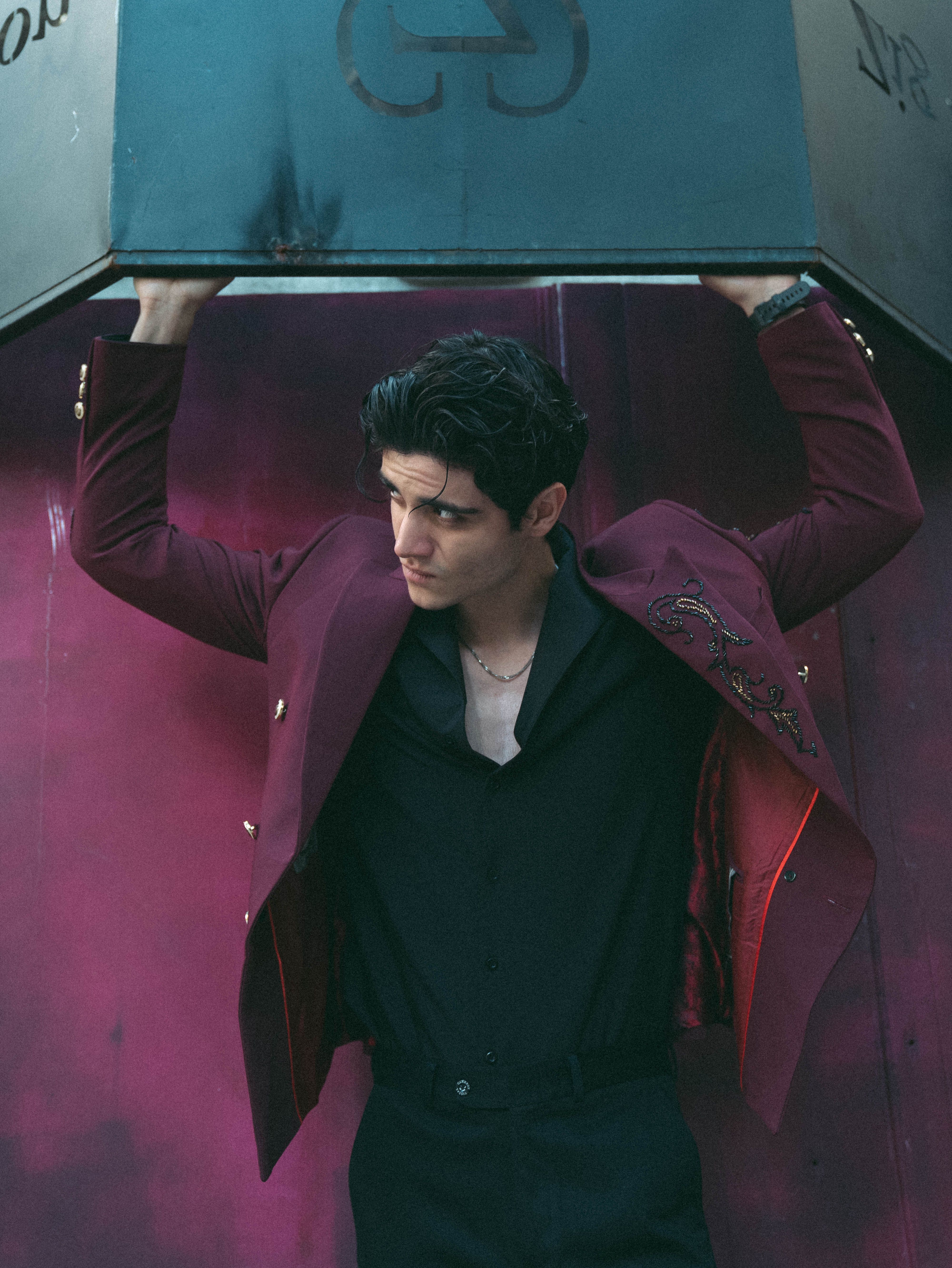 Confident man in a maroon jacket lifting a heavy object indoors with a strong pose.