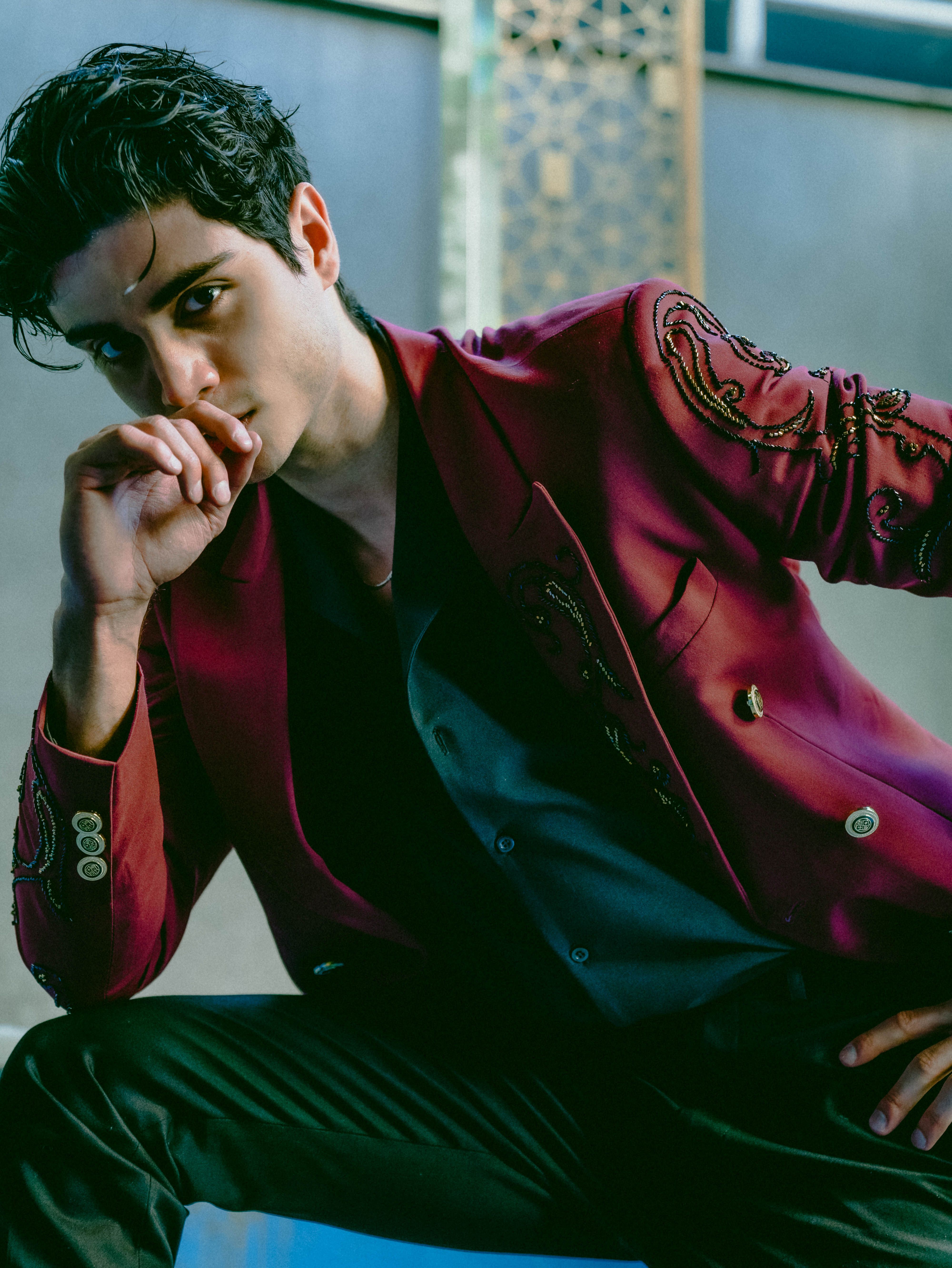 Confident young man in an embroidered red jacket posing in a sophisticated indoor setting.