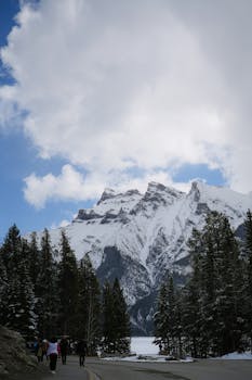 A majestic snowy mountain scene with people walking through a forest valley, perfect for travel themes.