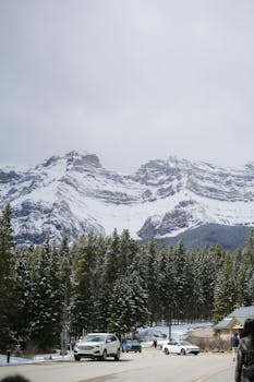 Snow-covered mountains and pine trees in Banff National Park, Canada, with cars on a winter road.