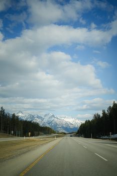 A wide open road leads to breathtaking snow-capped mountains under a vibrant blue sky.