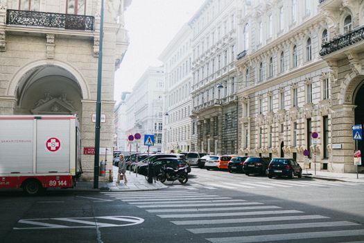 A bustling Vienna street with classic architecture, cars, and pedestrians under bright daylight.