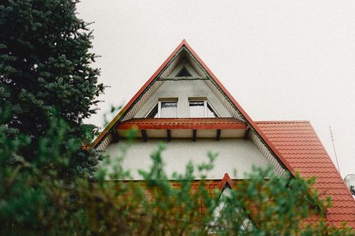 Free Charming house with a distinct red triangle roof surrounded by greenery, showcasing unique architecture. Stock Photo