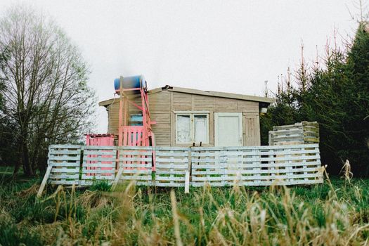 Charming rustic wooden cabin surrounded by nature, featuring a colorful fence and rural landscape.