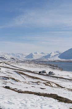 Remote cabin nestled in snowy mountains under a clear sky, showcasing serene winter scenery.