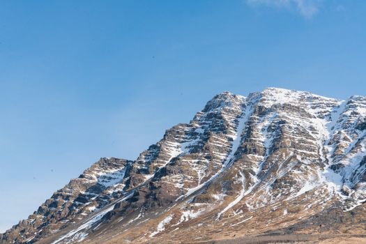 Majestic snow-covered mountain peak under a bright blue sky, showcasing pristine nature.