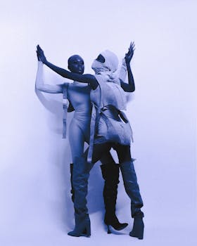Two fashion models in avant-garde outfits striking a dynamic pose against a minimalist background.