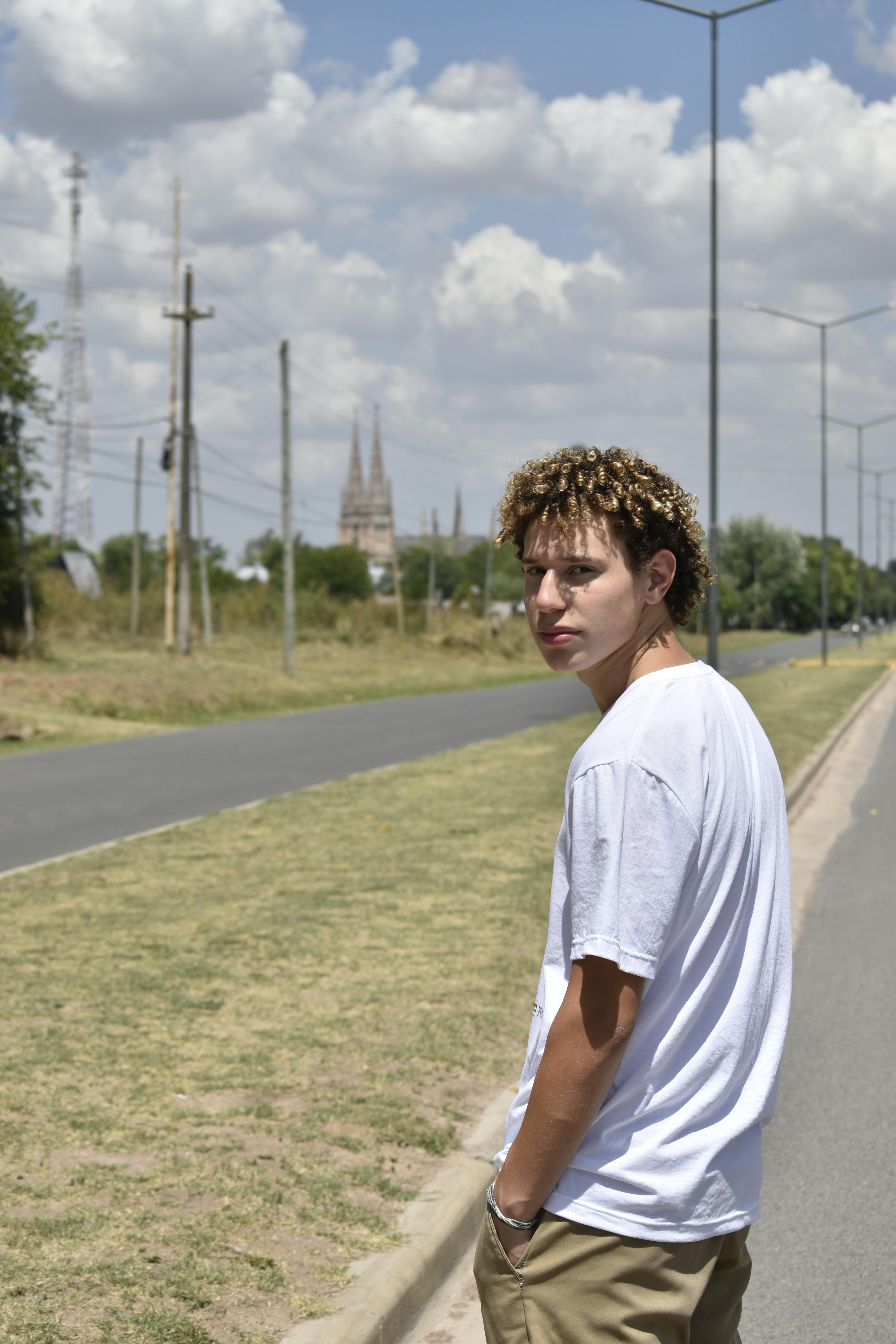 Casual young man walking outdoors on a sunny day near a country road.