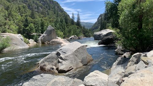 Free View of tranquil river surrounded by granite boulders and lush forest in Yosemite National Park, California. Stock Photo