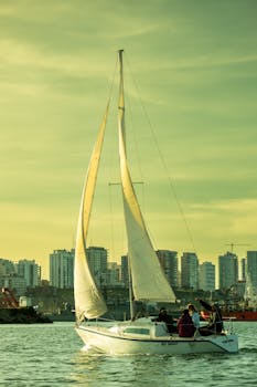 A sailing boat glides on the water during sunset in Mar del Plata with a city skyline backdrop.