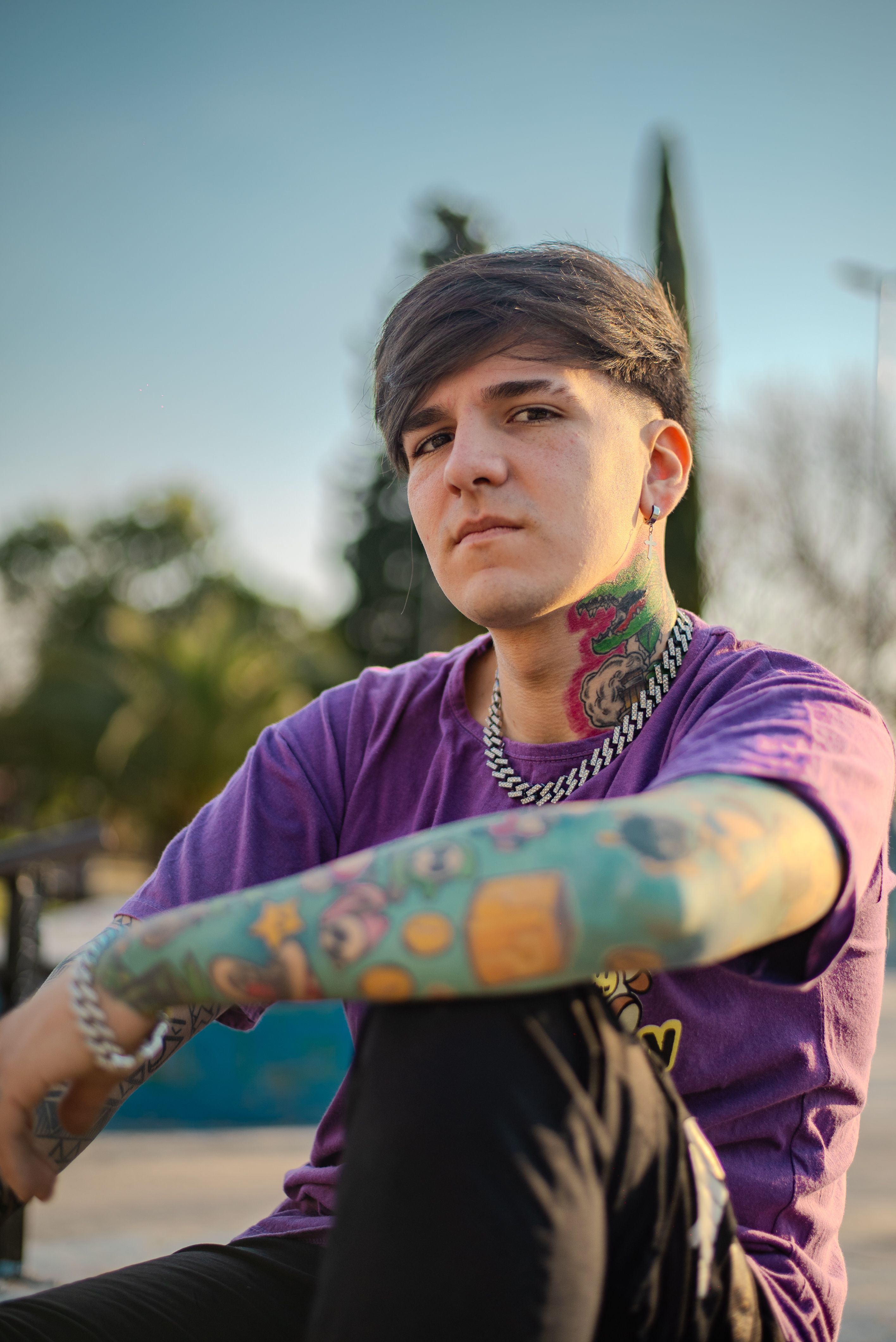Young tattooed man with colorful tattoos sits outdoors, exuding a casual and modern style.