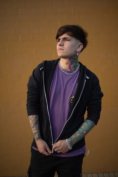 Free A young man with vibrant tattoos poses against an urban brick wall, showcasing modern style. Stock Photo