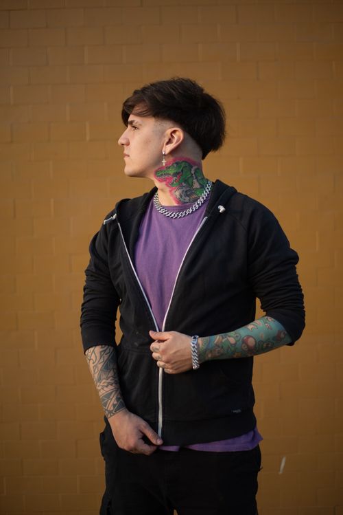 Free Young man with vibrant tattoos stands against a yellow wall, showcasing street fashion style. Stock Photo