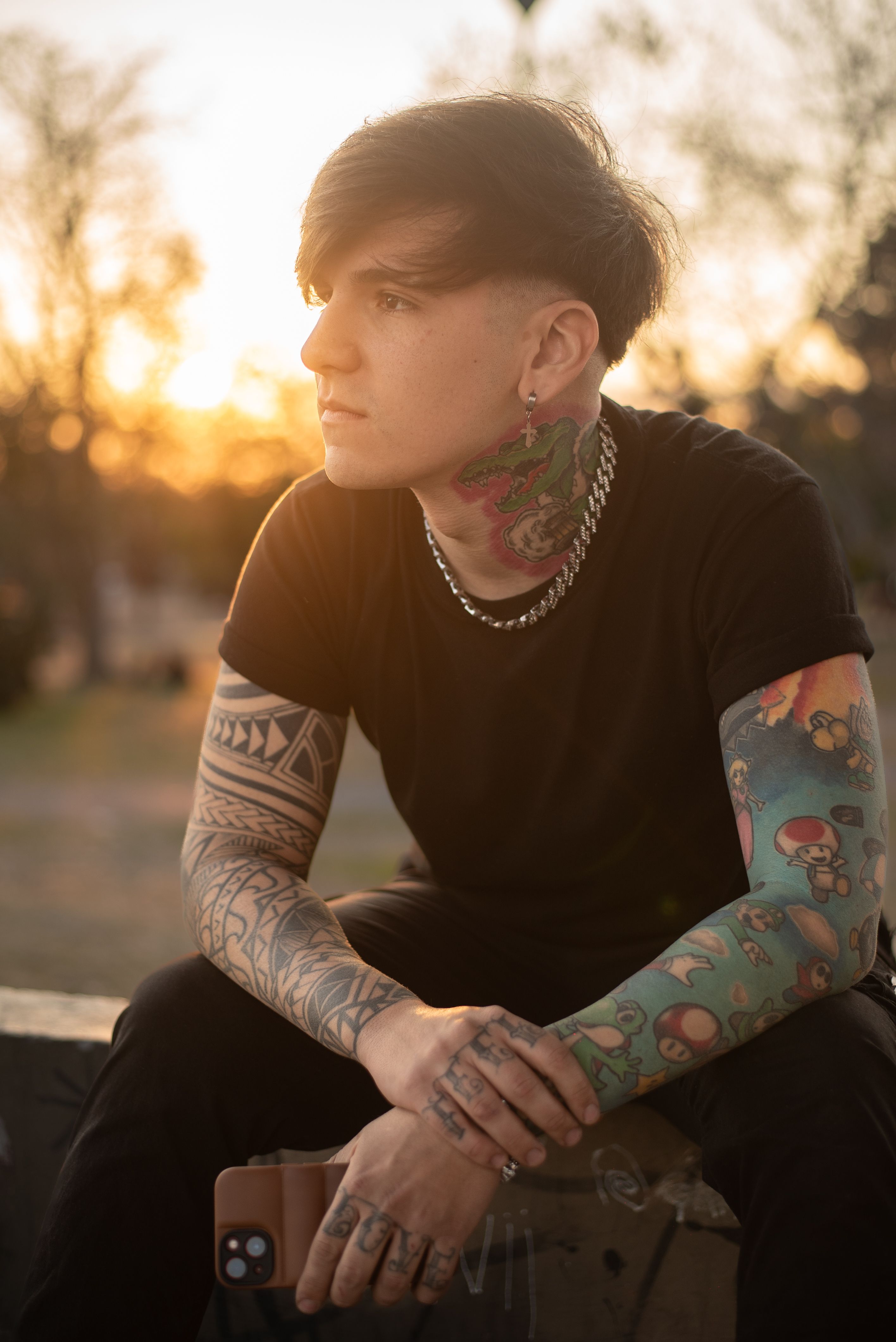 A tattooed individual sitting outdoors, contemplating at sunset, blending art and nature.