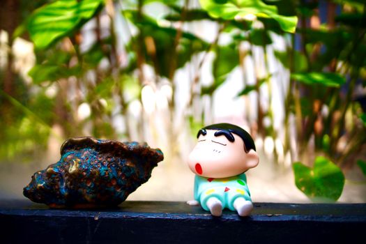 Toy character figurine beside a large shell in a lush outdoor setting.