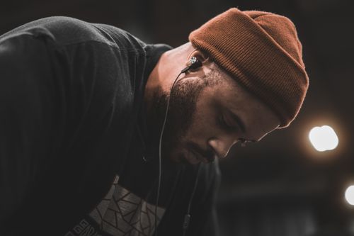 Free A man with a beanie and earphones is intently focused in dim lighting, creating a moody atmosphere. Stock Photo