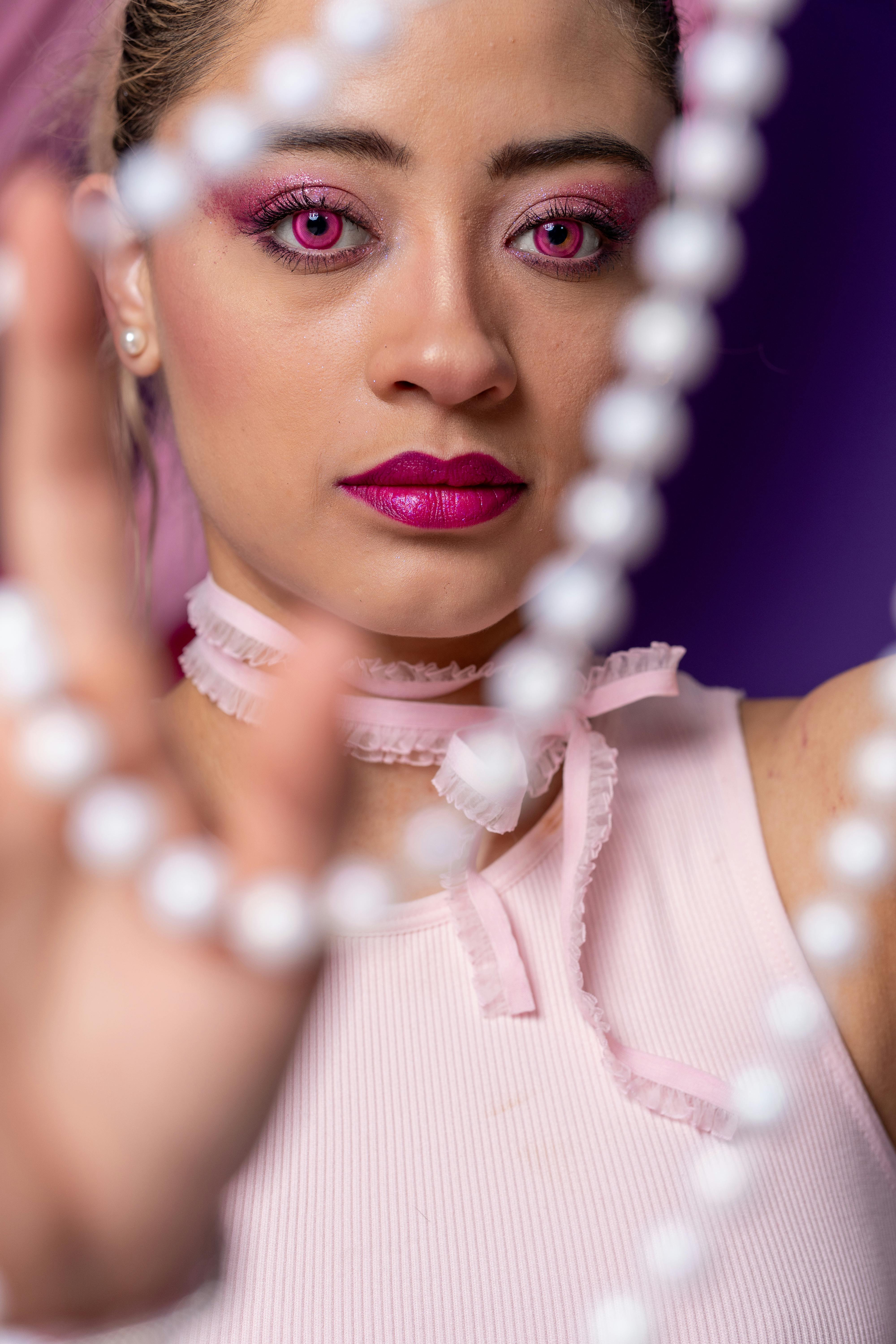 Close-up portrait of a woman in pink with pearls, vibrant makeup, and accessories.