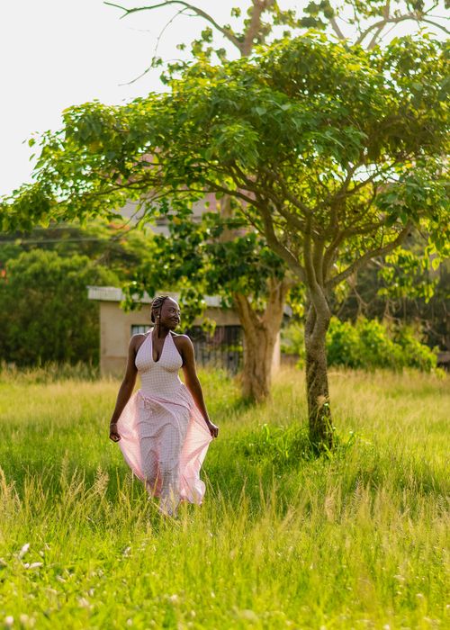 Free A woman in a white dress enjoys a sunny day in a lush green field under a tree. Stock Photo