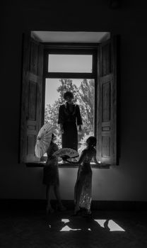 Three people silhouetted in a window with parasols, creating dramatic shadows in black and white.