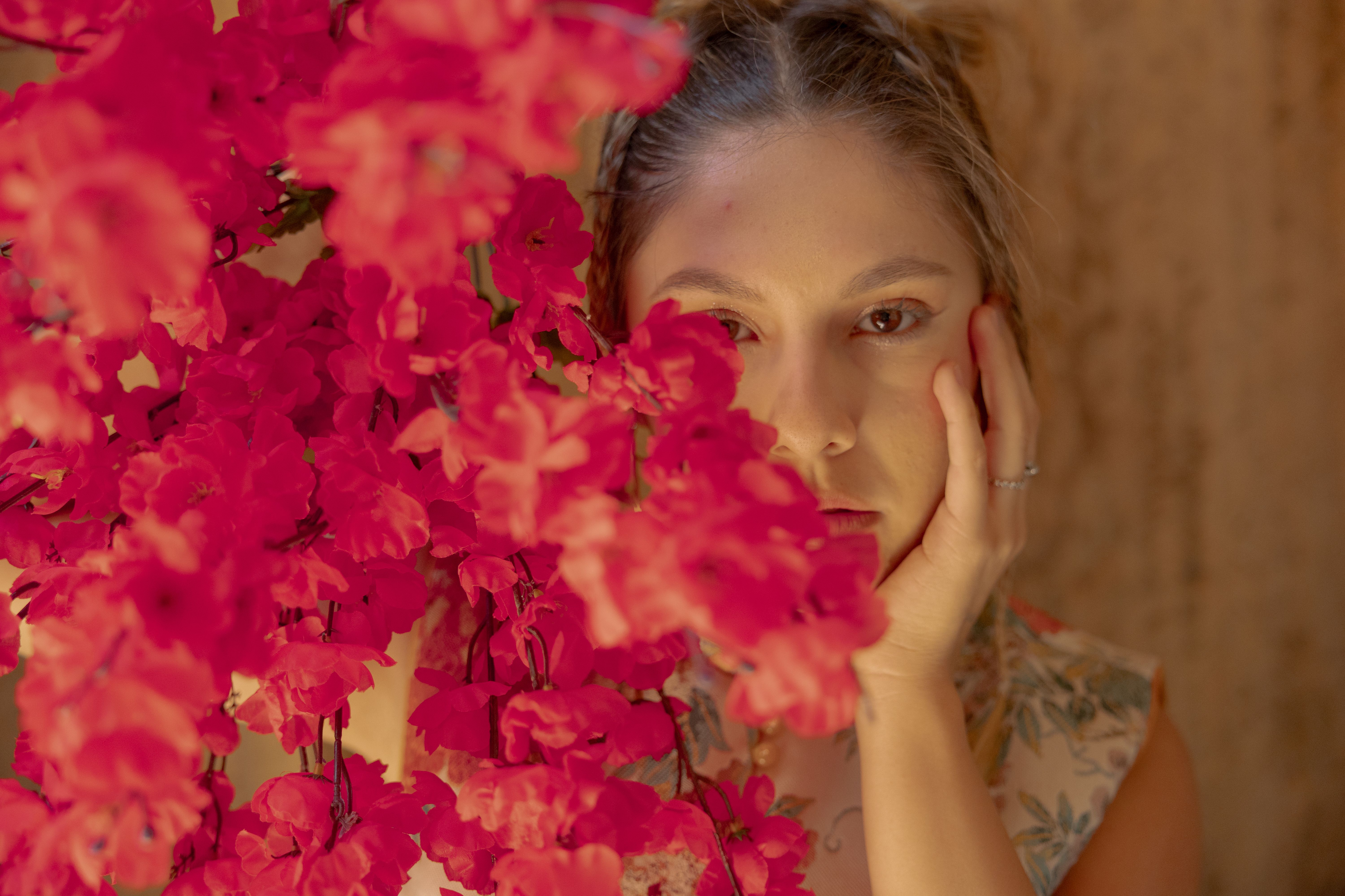 Portrait of a Woman Behind Vibrant Red Flowers · Free Stock Photo