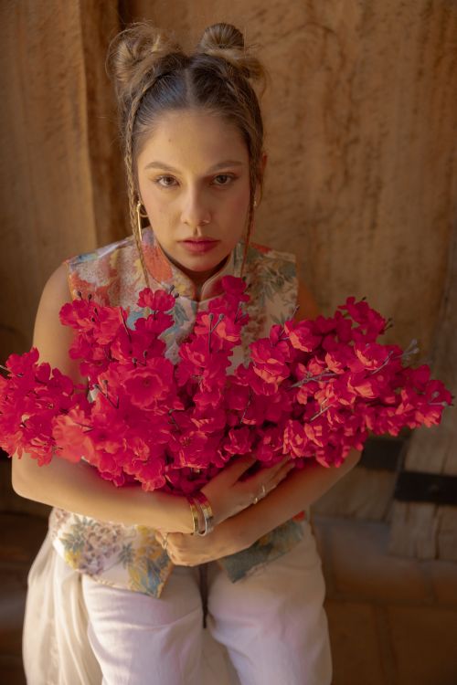 Free Young woman holding vibrant red flowers indoors with a rustic backdrop, exuding a serene and warm mood. Stock Photo