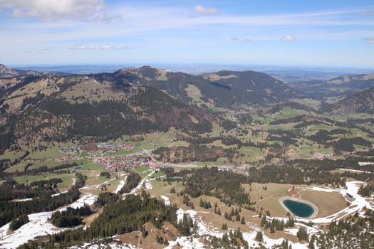 Breathtaking aerial shot of Austrian landscape with snow patches, fields, and mountains.