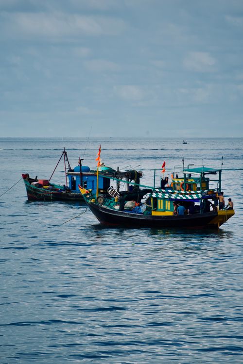 Free Traditional fishing boats with vibrant colors anchored in a tranquil sea under a cloudy sky. Stock Photo