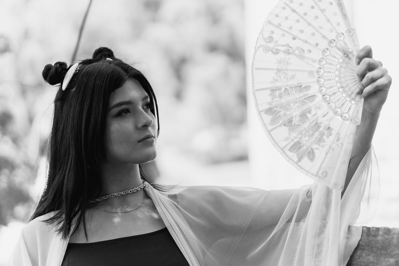 black and white portrait of a woman holding an ornate fan creating an
