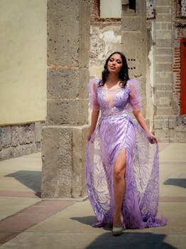 A woman poses elegantly in a detailed purple dress against a historic architecture backdrop.
