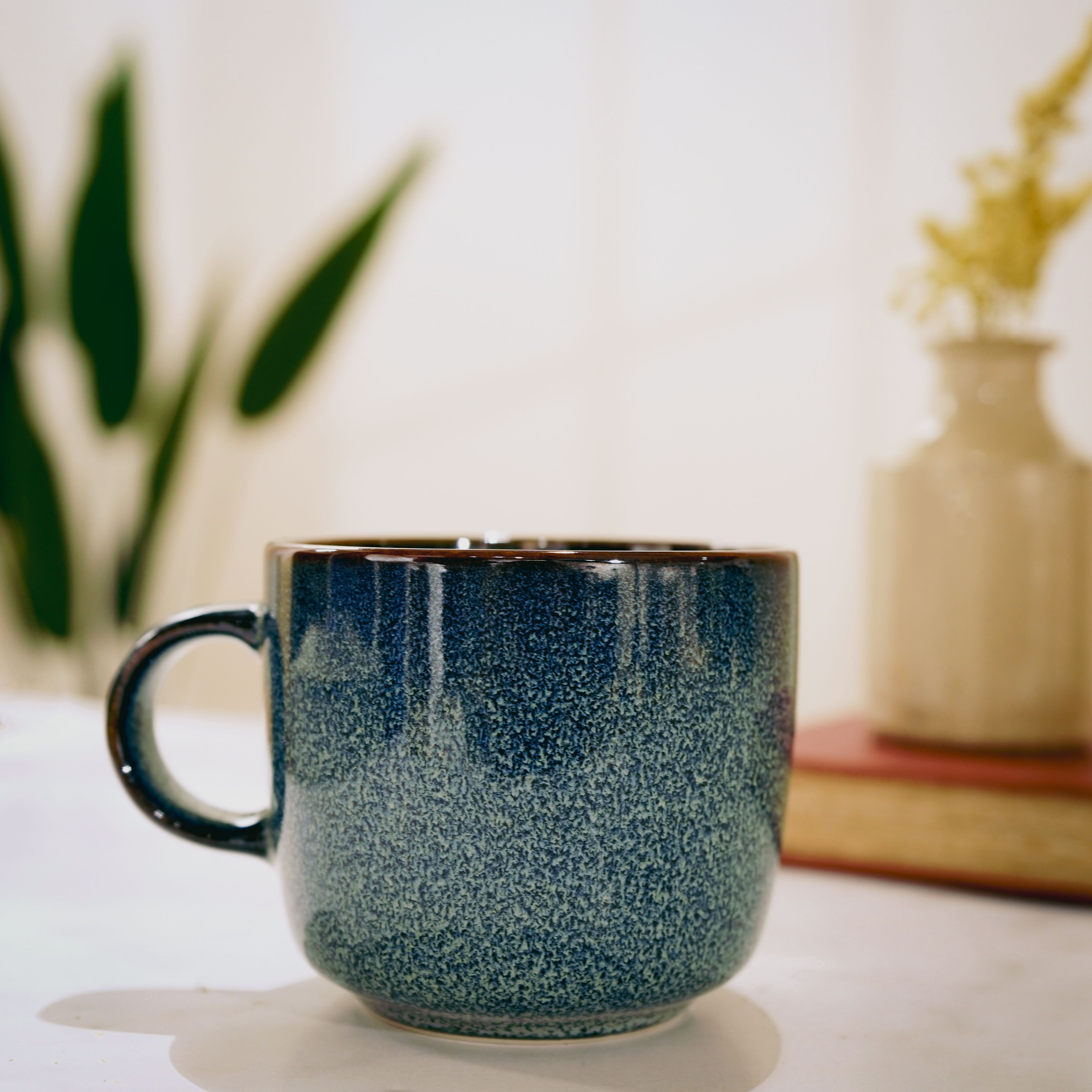 A blue ceramic mug with a vintage aesthetic placed on a surface indoors, evoking a cozy atmosphere.