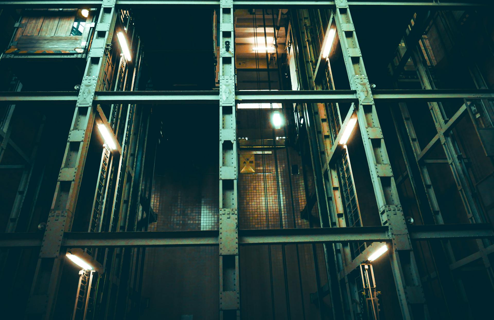 A dimly lit industrial elevator shaft with metal framework and lights.