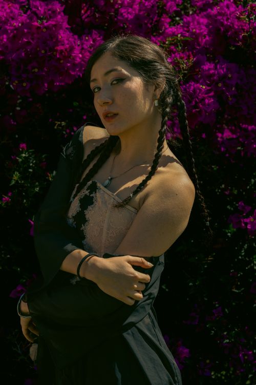 Free A woman with braided hair poses gracefully against vibrant purple flowers Stock Photo