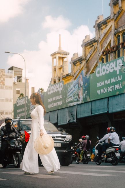 Woman in traditional white dress crossing a busy street with historic buildings.