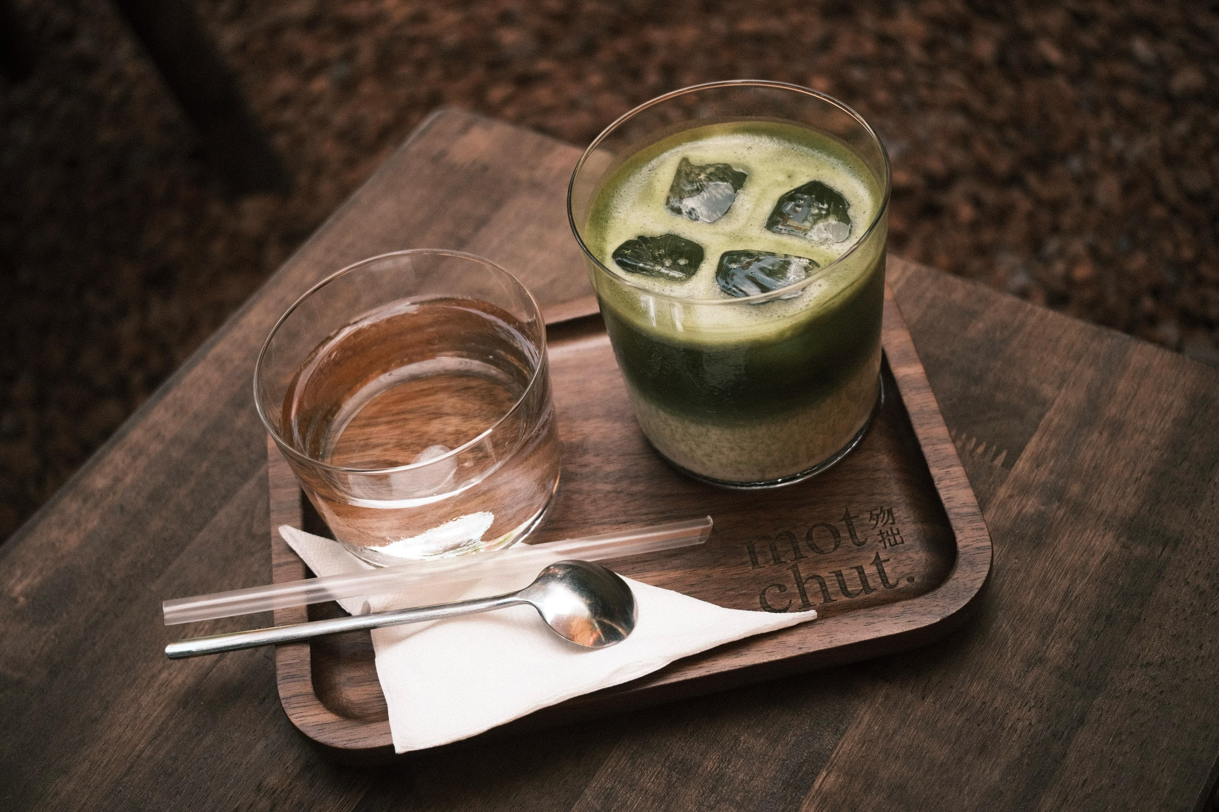 A delightful matcha iced beverage served alongside water on a wooden tray.