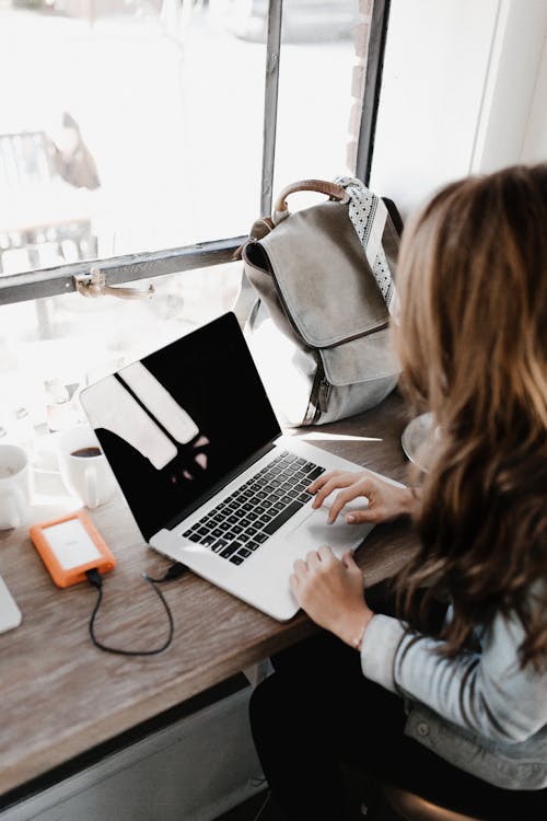 Fotografi Close Up Wanita Yang Duduk Di Sebelah Meja Saat Menggunakan Macbook