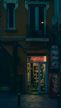 A cozy, warm-lit barber shop at night with neon lights glowing in an urban street.