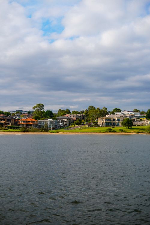 Free A picturesque view of suburban coastal homes with a serene water body under a cloudy sky. Stock Photo