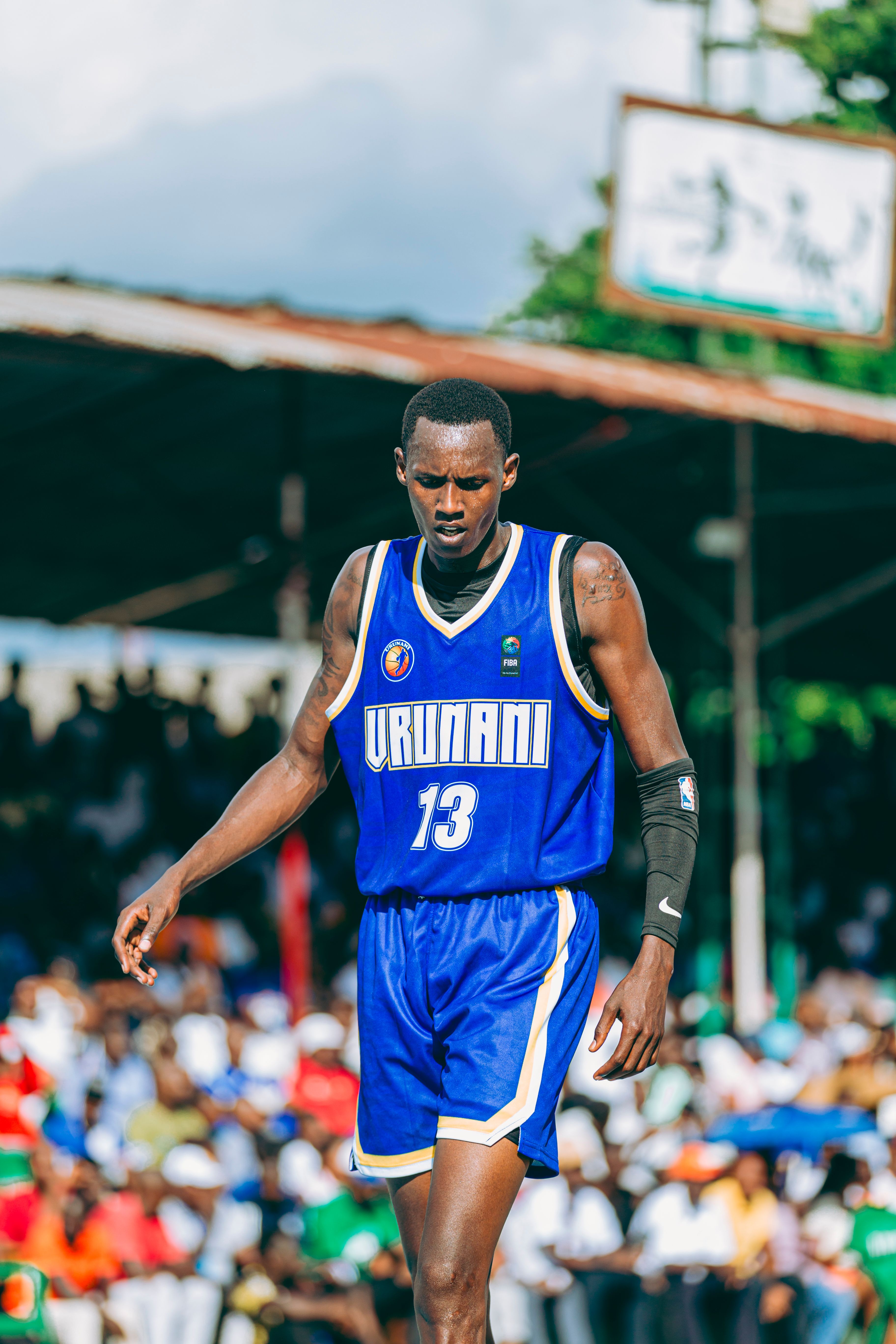 Focused basketball player wearing blue jersey during outdoor game with crowd watching.
