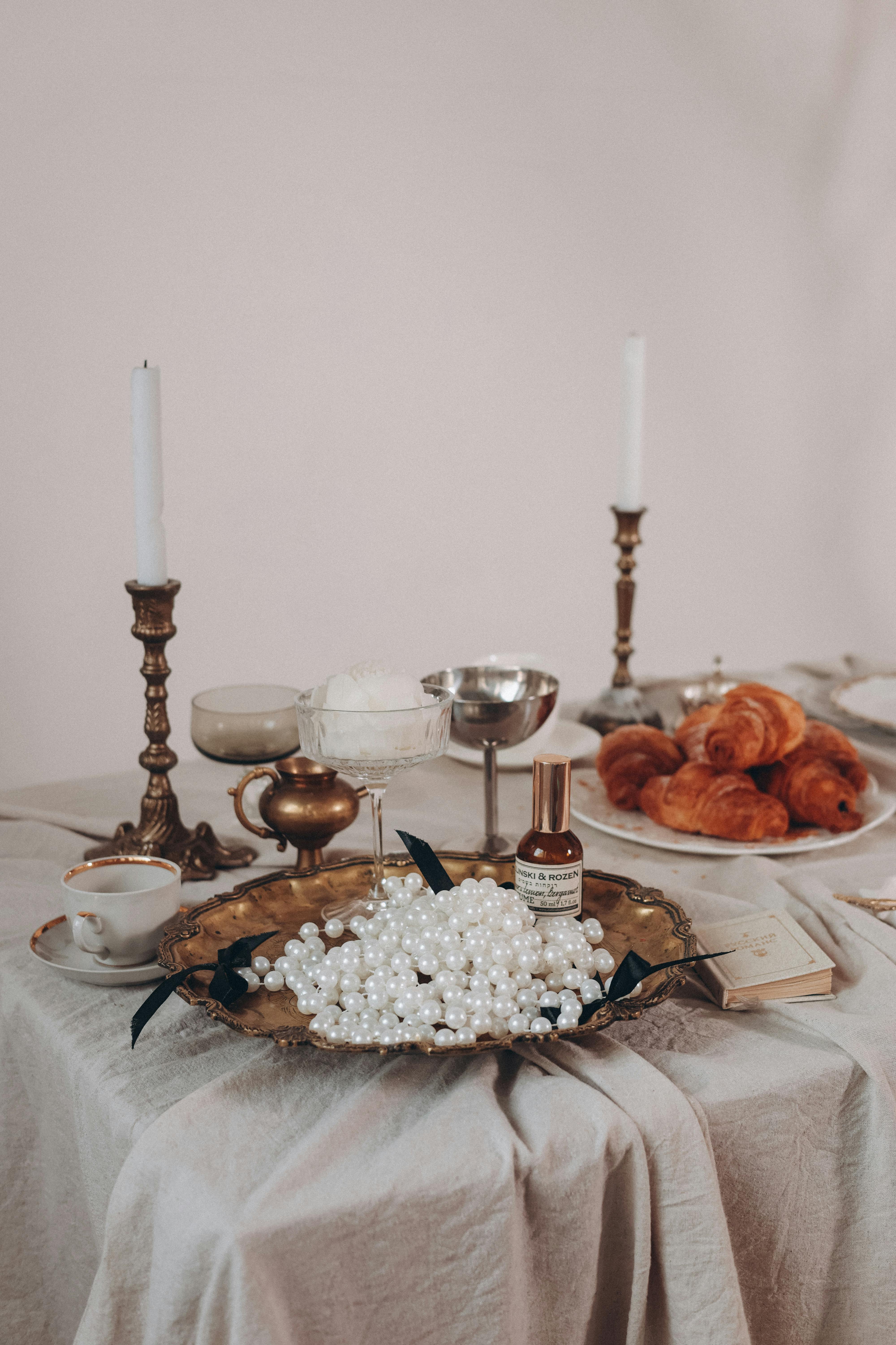 A luxurious table setting featuring pearls, croissants, and vintage candle holders, exuding elegance.