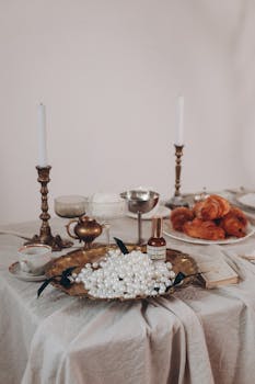 A luxurious table setting featuring pearls, croissants, and vintage candle holders, exuding elegance.