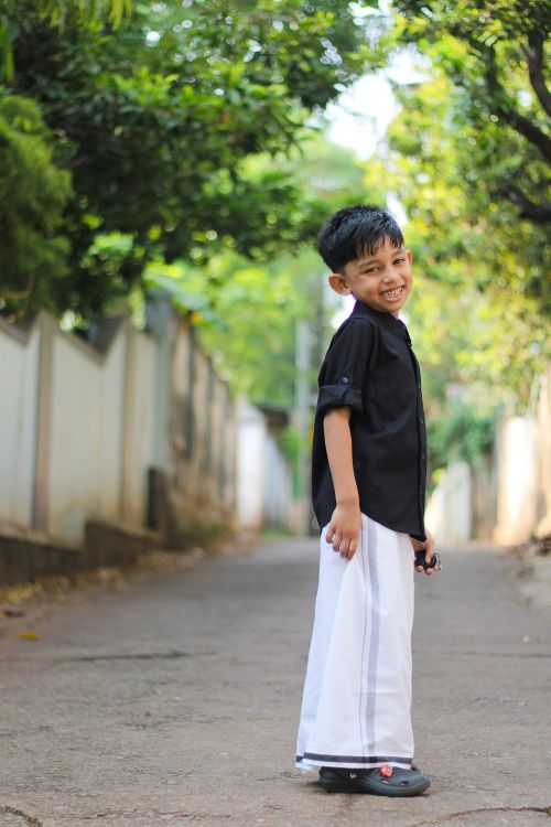 Free A cheerful boy in traditional Kerala dress standing in a leafy street, exuding happiness. Stock Photo