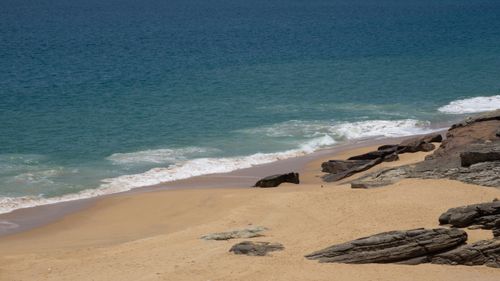 Free A serene sandy beach with gentle waves and rocky outcrops, perfect for relaxation and coastal exploration. Stock Photo